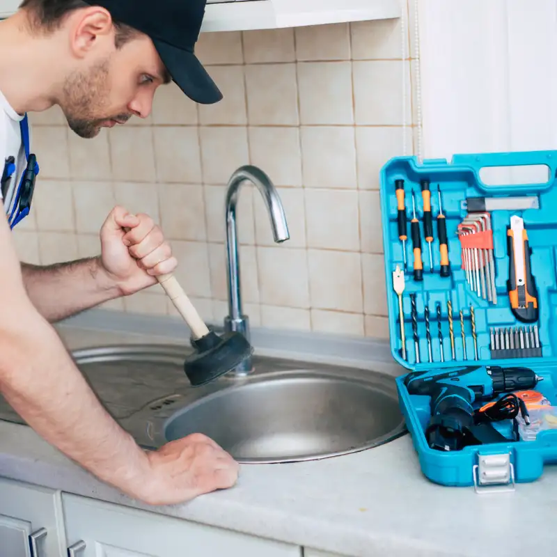 Plumber using a plunger on a clogged kitchen sink